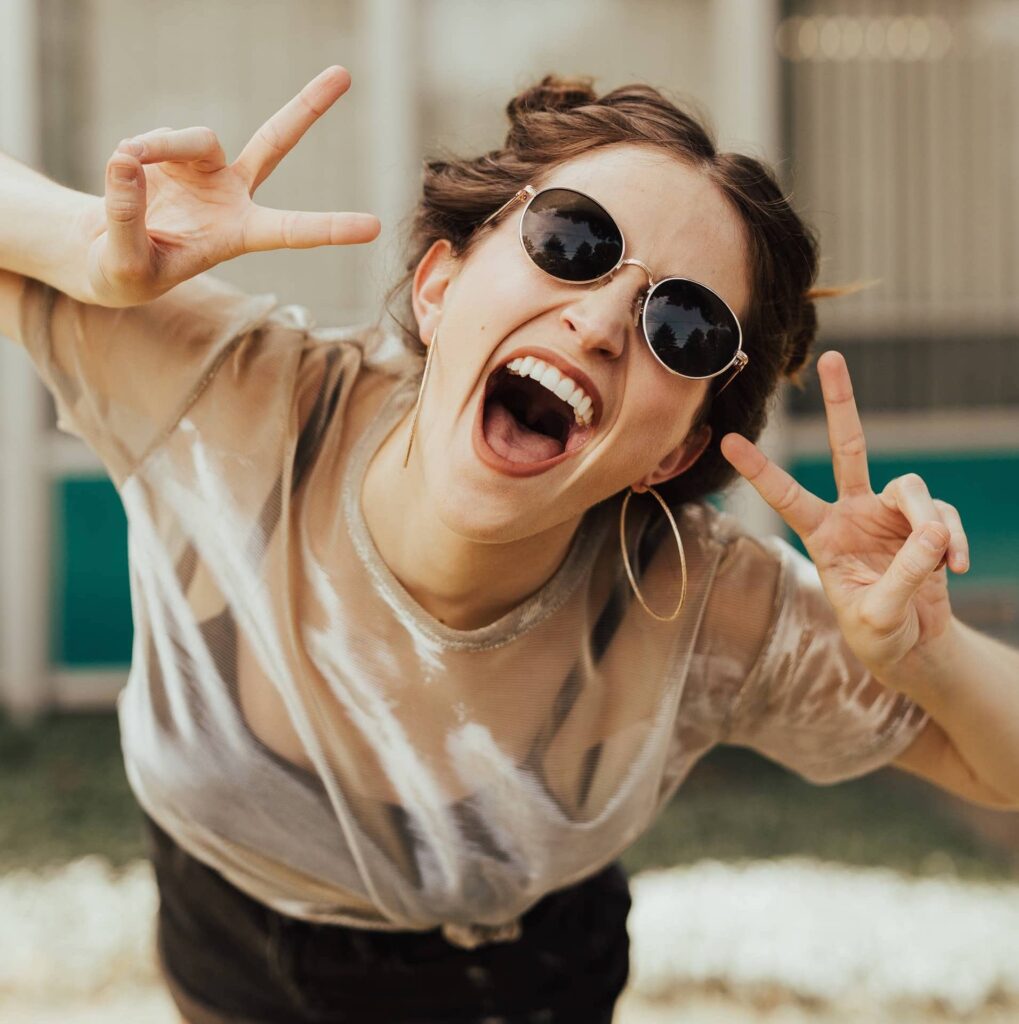 Sonnenbrille lächelt mit Victoryzeichen in Kamera